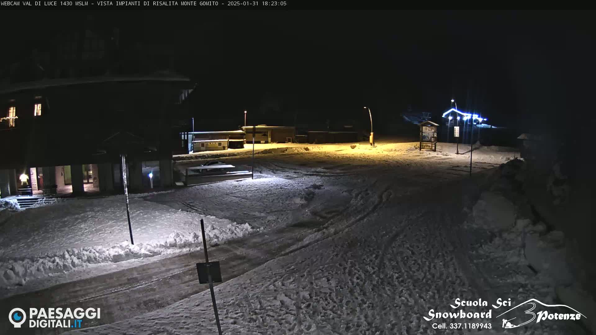 A snow-covered nighttime scene shows a road and buildings illuminated by artificial light.