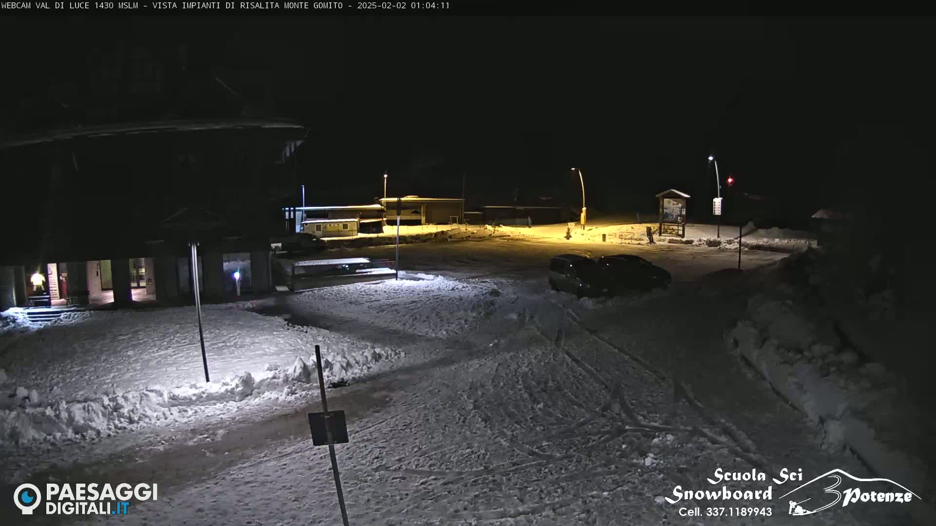 A nighttime scene of a snow-covered parking lot and building, illuminated by artificial lights.