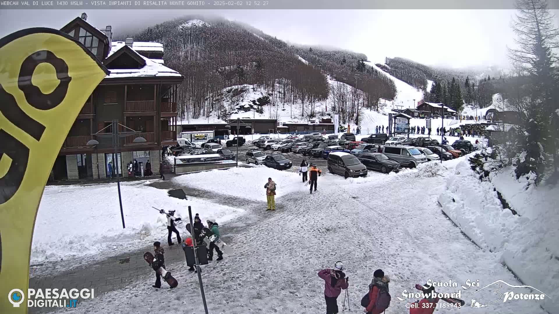 A snow-covered parking lot and a multi-story building are seen next to a ski slope on an overcast day.
