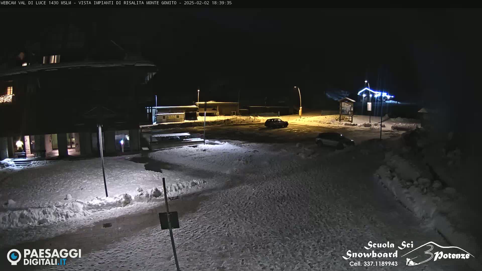 A snow-covered parking lot and buildings are illuminated at night.