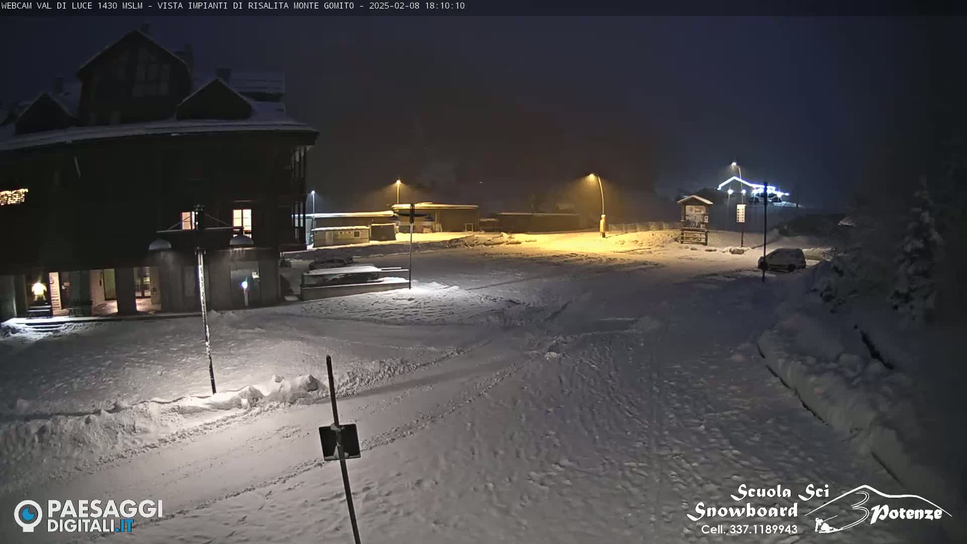 A snow-covered parking lot and building are illuminated at night under hazy conditions.