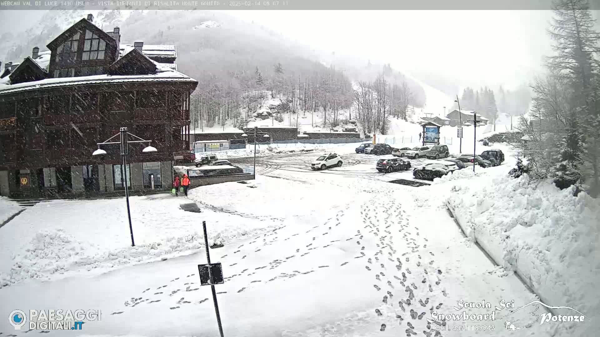 A snow-covered parking lot and building are visible, with fresh footprints in the snow and a light snowfall occurring.
