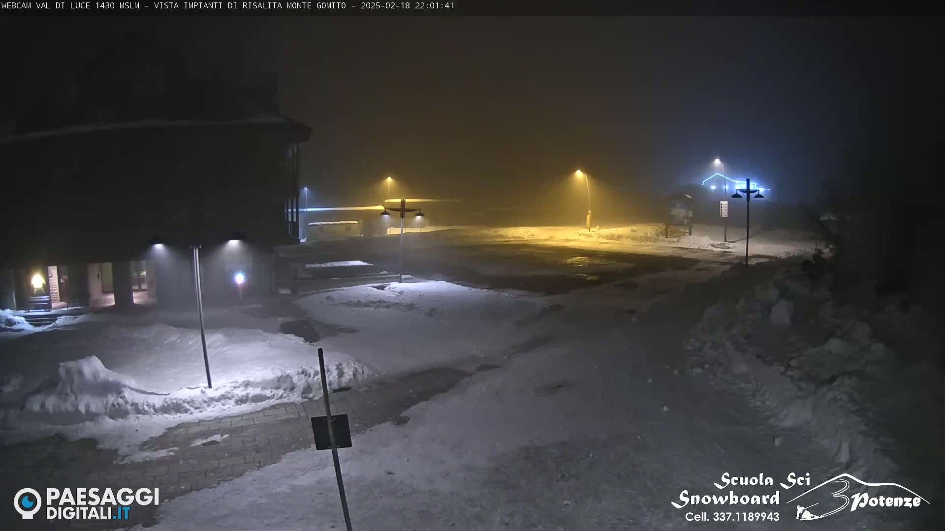 A snow-covered parking lot is dimly lit by streetlights under a foggy night sky.