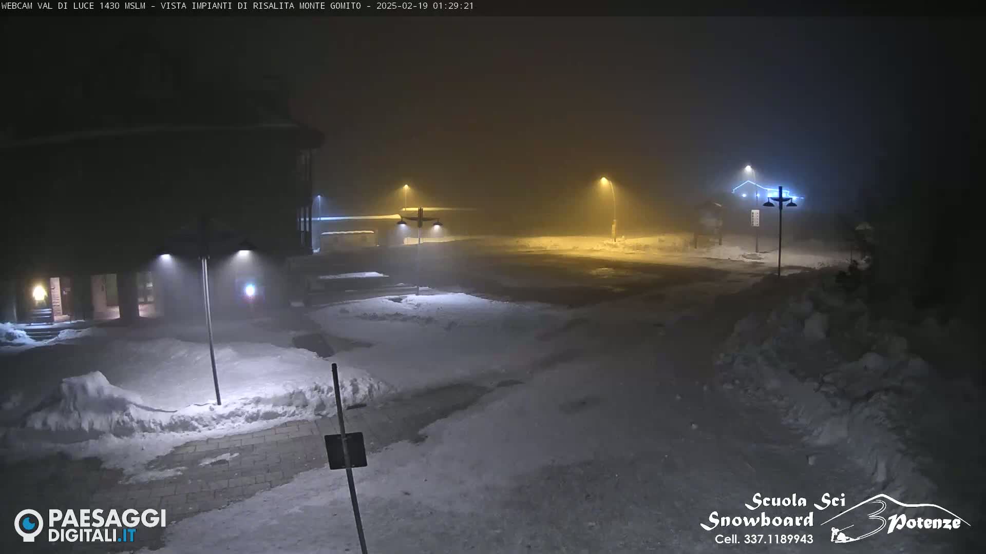 A snow-covered area at night is dimly lit by streetlights in foggy conditions.