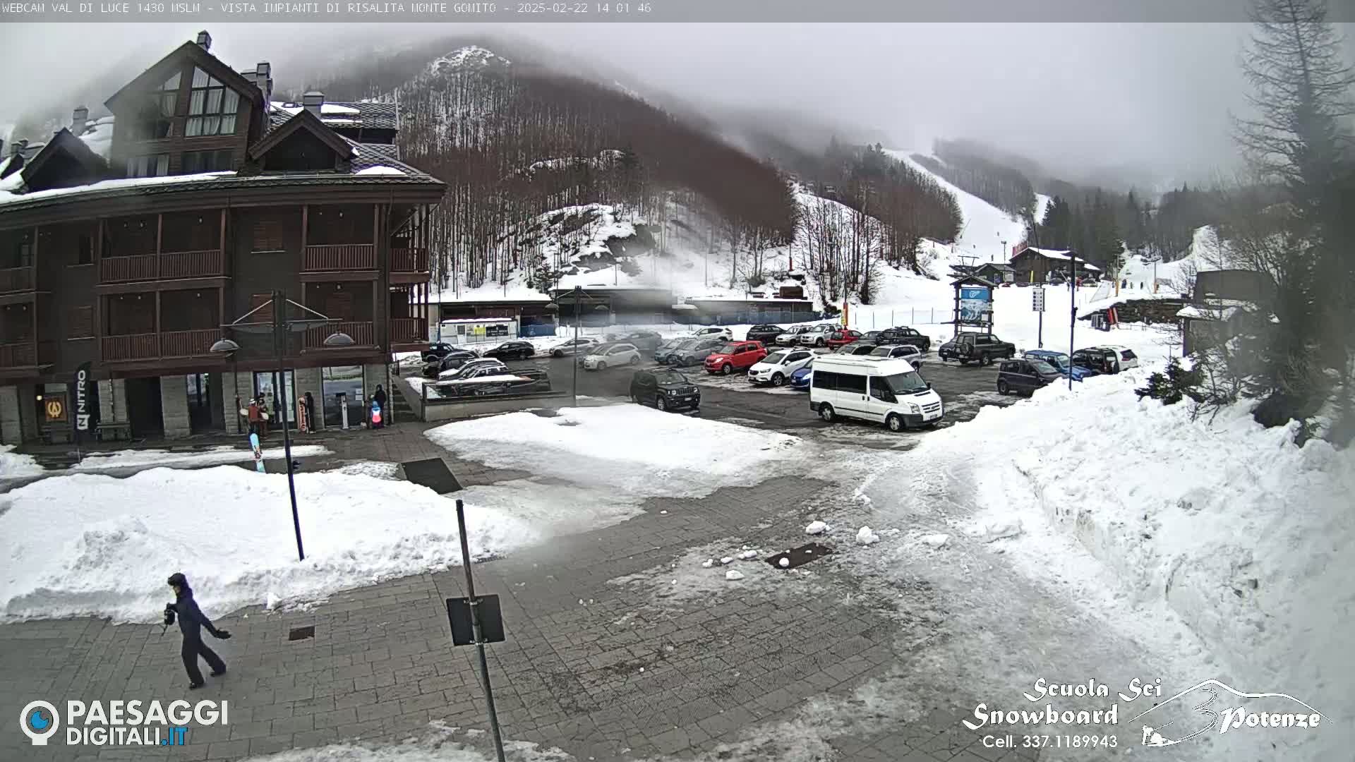 A snow-covered parking lot and plaza sit in front of a multi-story building, with a misty mountainside visible in the background.
