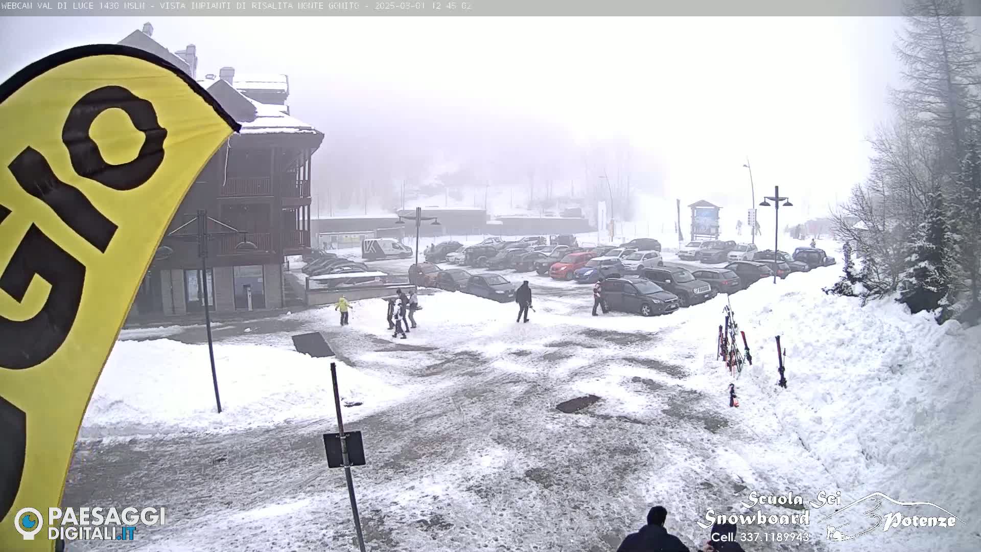 A snowy parking lot with several cars and a few people walking, situated in front of a building on a foggy day.