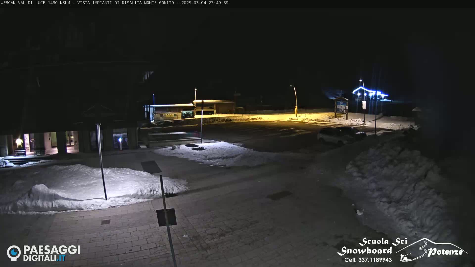 A snow-covered parking lot and surrounding buildings are illuminated at night.