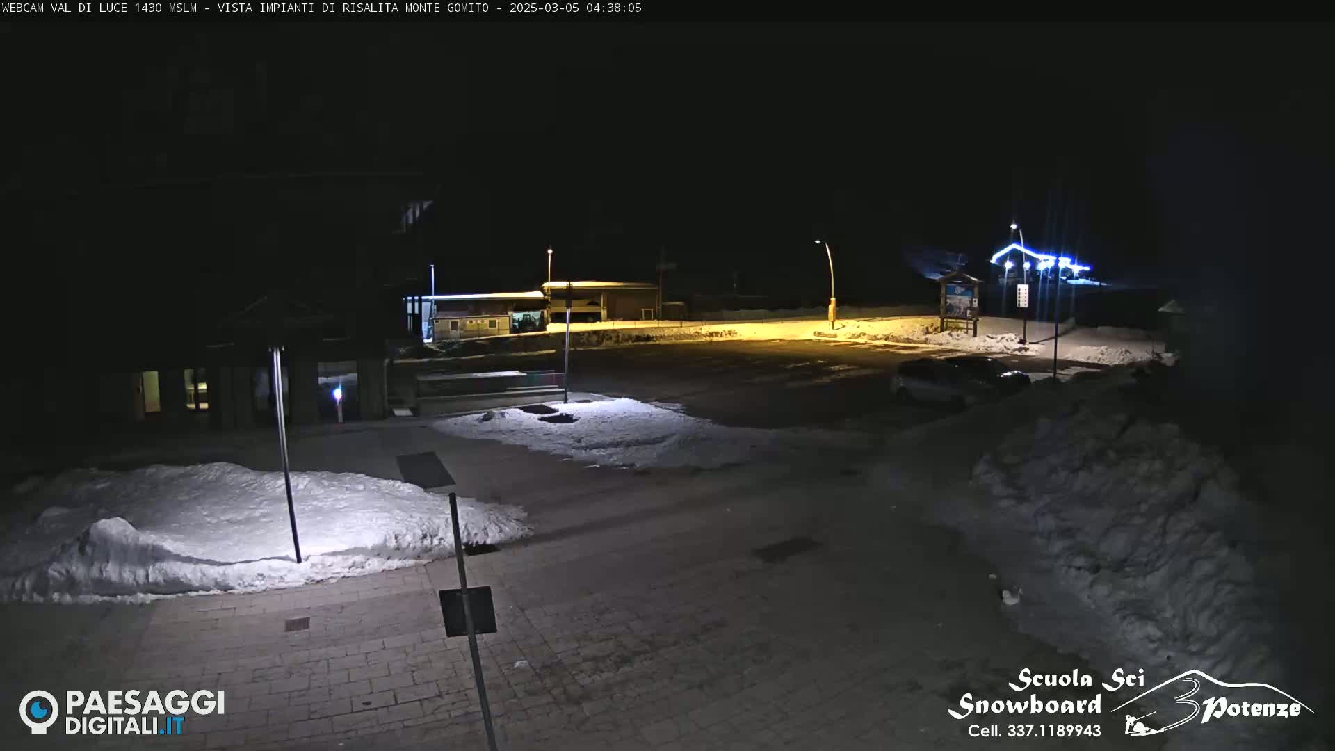 A nighttime view of a snow-covered parking lot and buildings, illuminated by artificial lights.