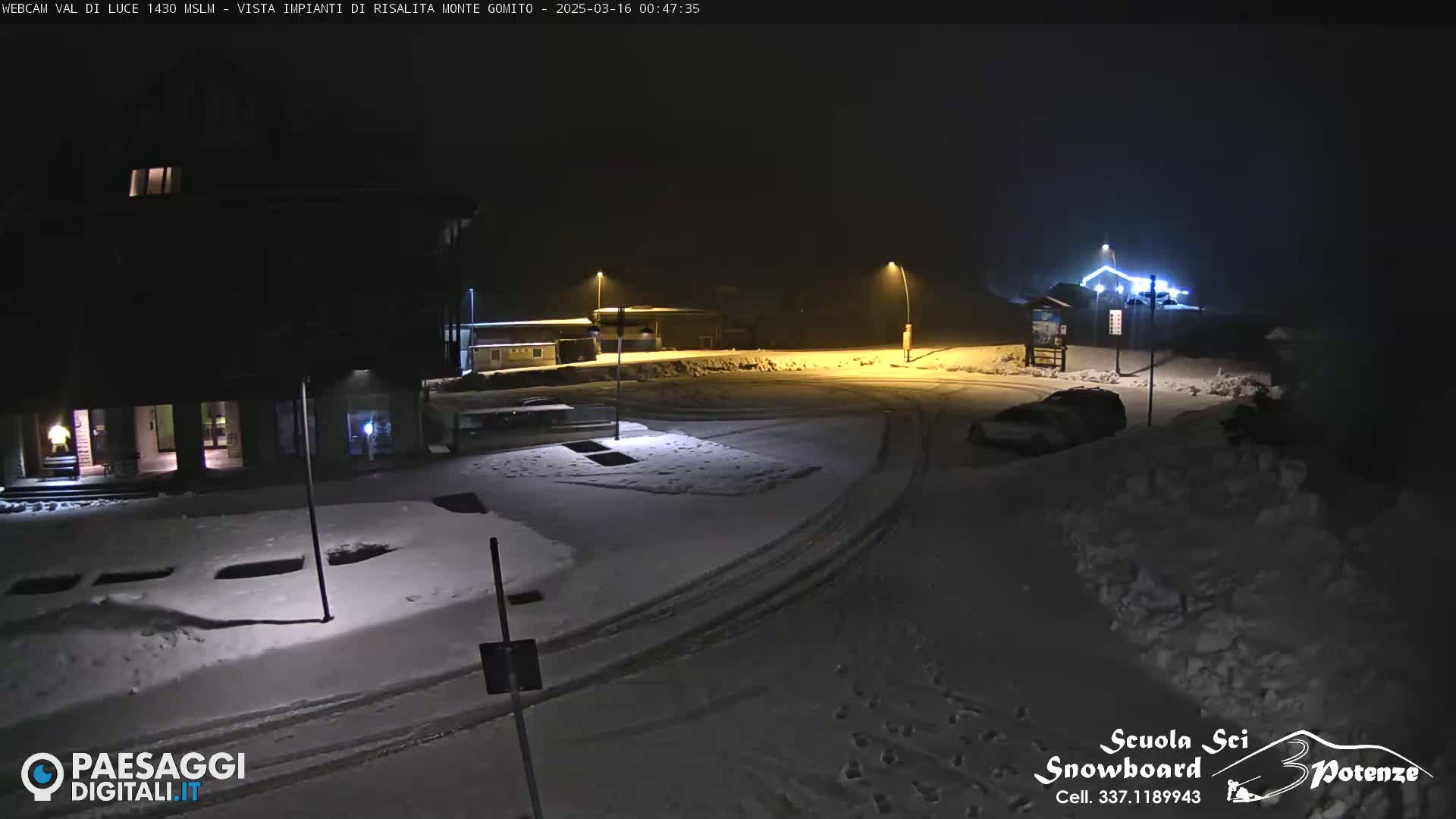 A snow-covered parking lot and buildings are illuminated at night by streetlights.