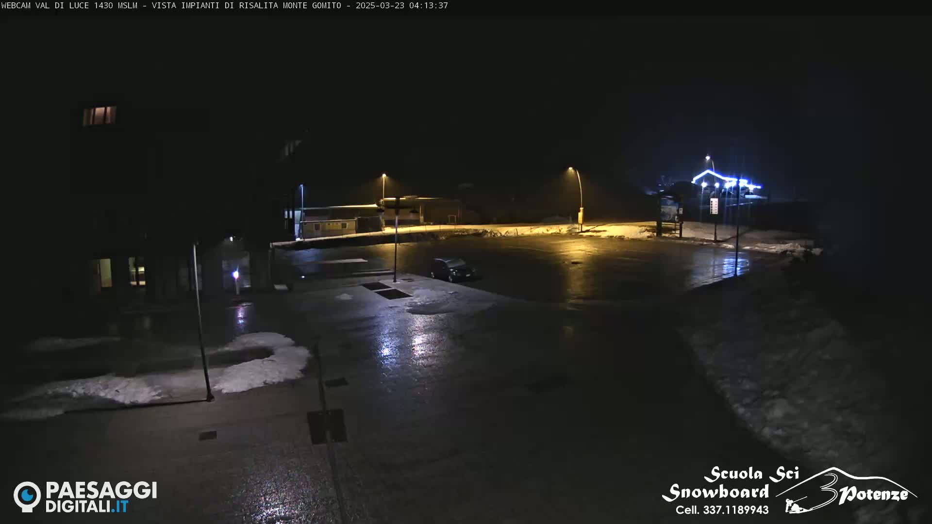 A nighttime view of a mostly empty parking lot with some snow on the ground and a few lights illuminating the scene.