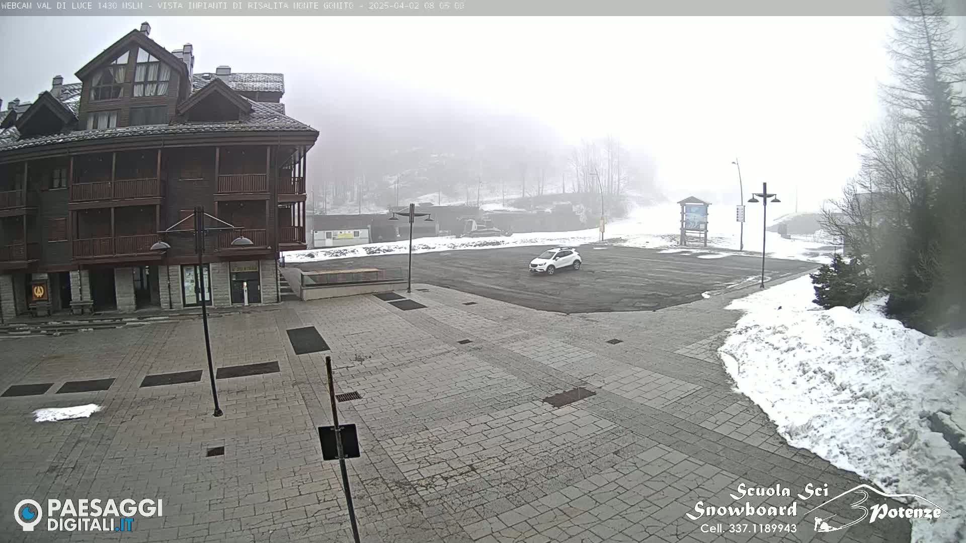 A snowy, foggy parking lot is situated in front of a multi-story brown building.
