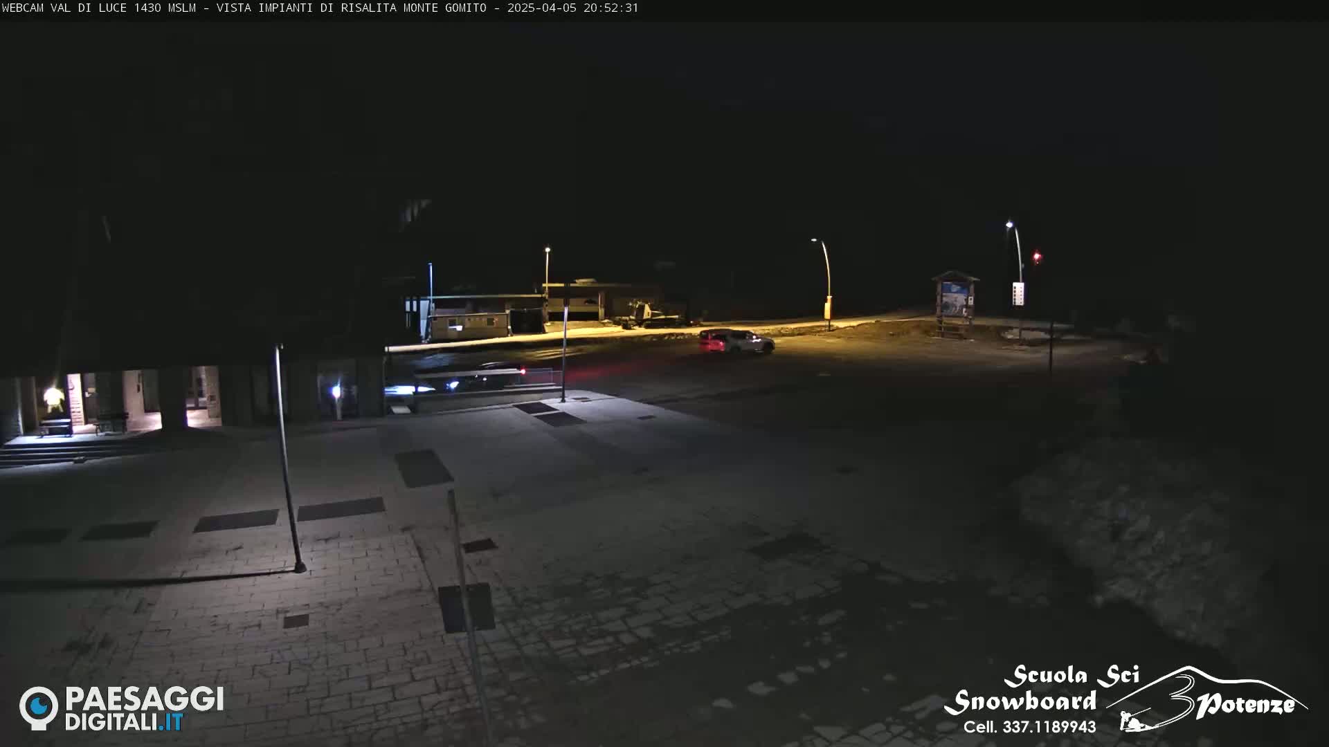 A nighttime view of a mostly empty paved area with a few vehicles, illuminated by streetlights.