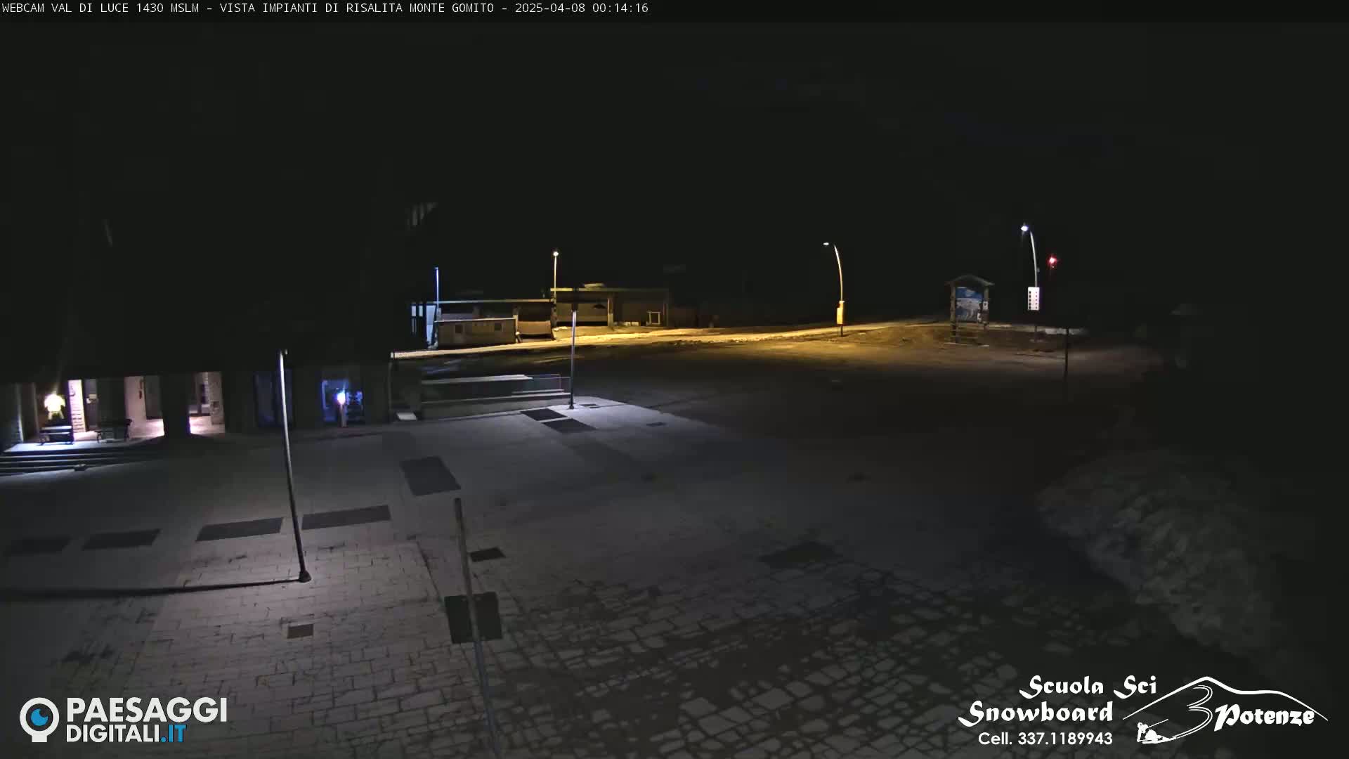 A dark, empty plaza at night, lightly dusted with snow, is illuminated by streetlights.