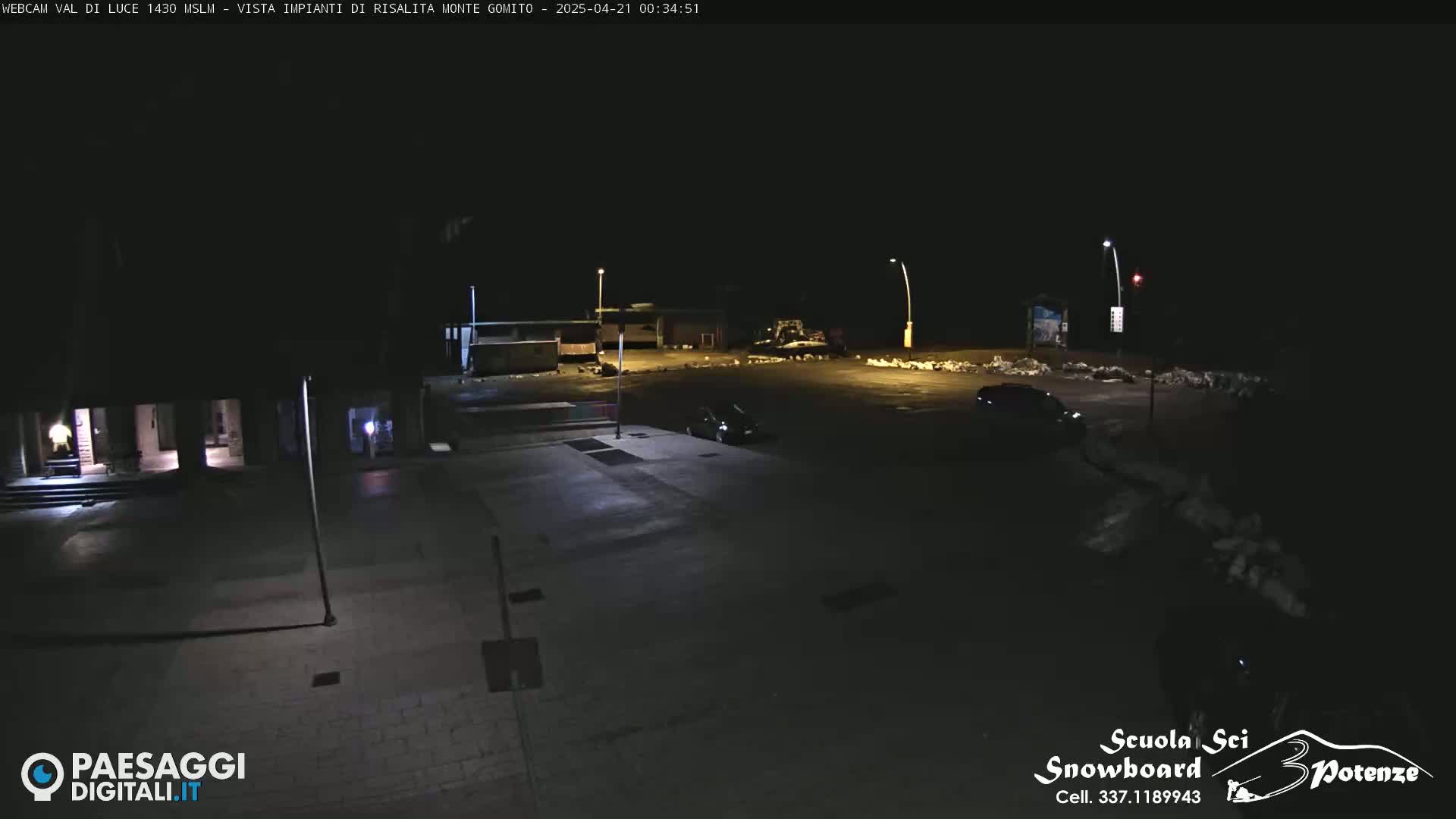 A nighttime view of a mostly empty parking lot and surrounding buildings illuminated by artificial lights.
