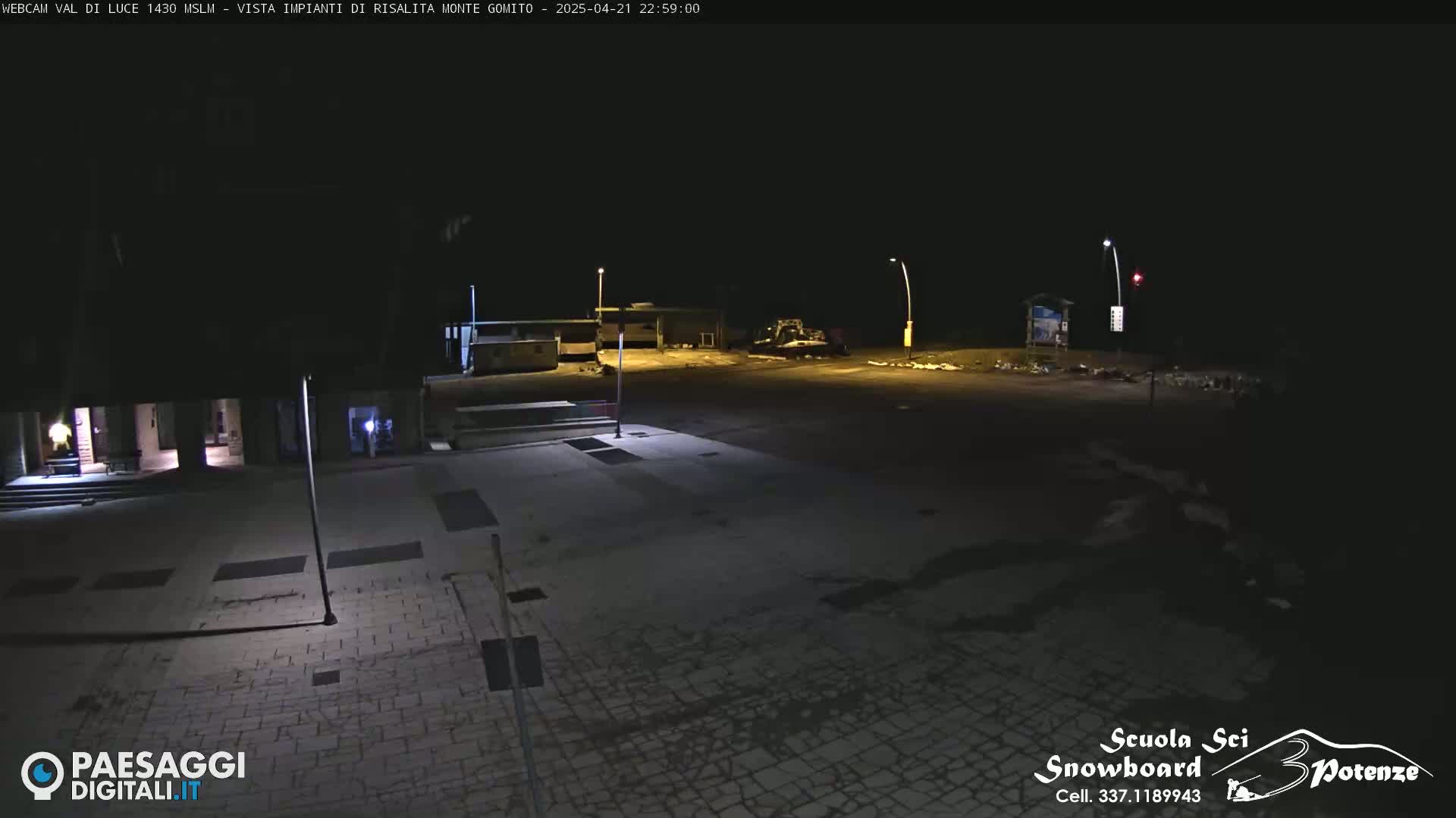 A nighttime view of an empty paved plaza with several buildings and some equipment visible in the distance.