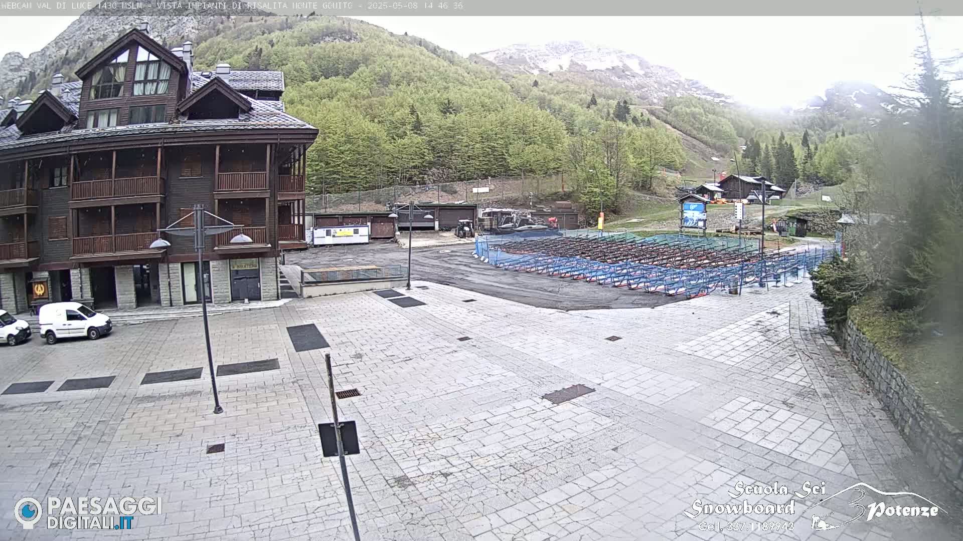 A stone plaza sits in front of a multi-story brown building, with numerous rows of what appears to be ski or snowboard racks in the background, under an overcast sky.