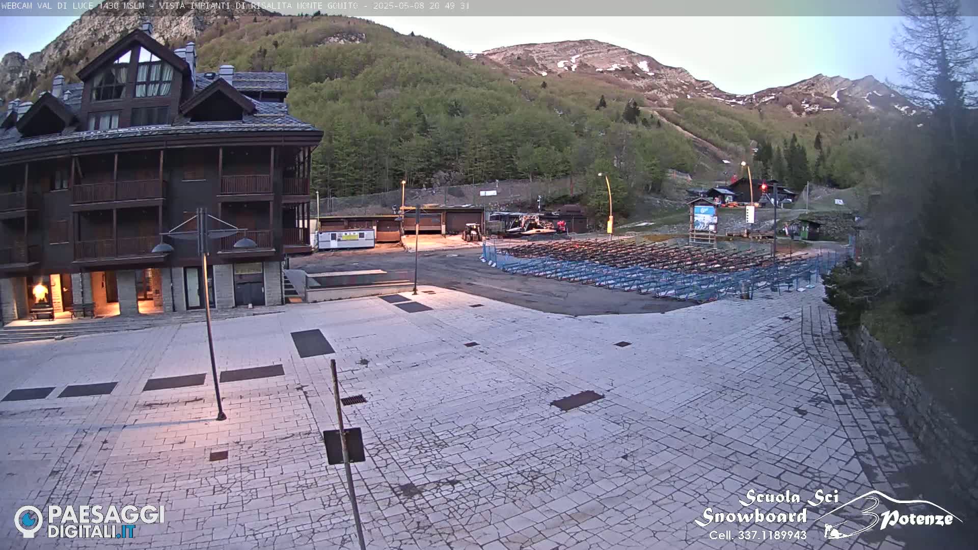 A stone plaza sits before a multi-story building, with a mountain backdrop under a twilight sky.