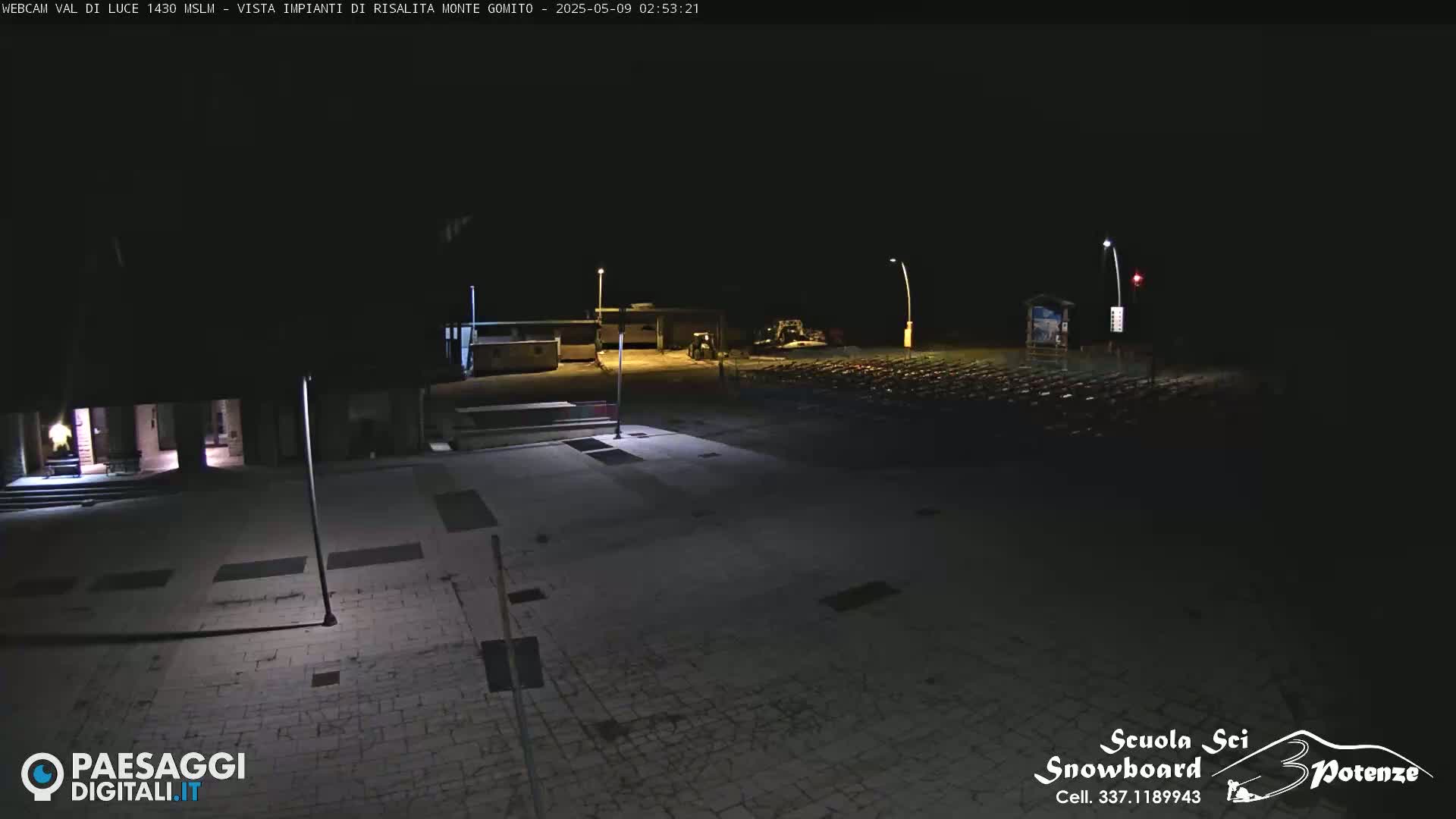 A nighttime view of a mostly empty paved plaza with some buildings and a few vehicles in the distance.