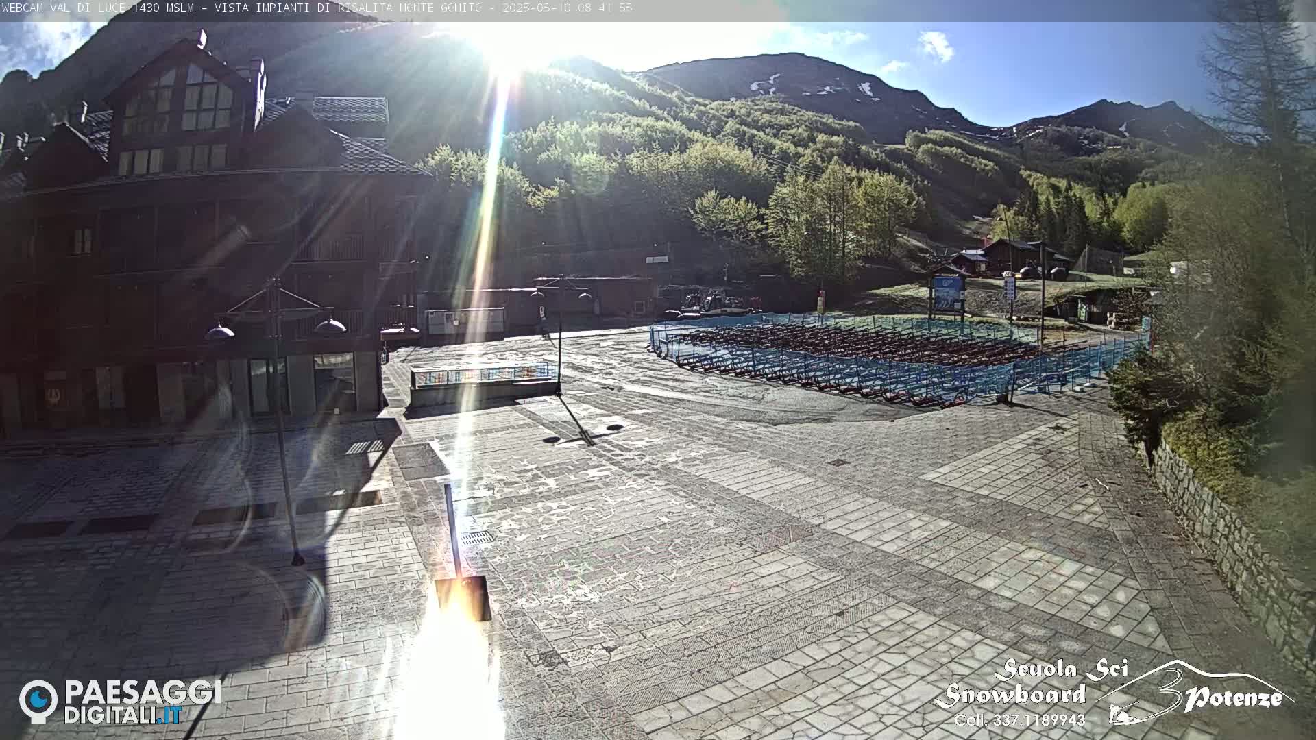A sunny day reveals a plaza with folded chairs, a building, and a mountainside covered in lush green trees.