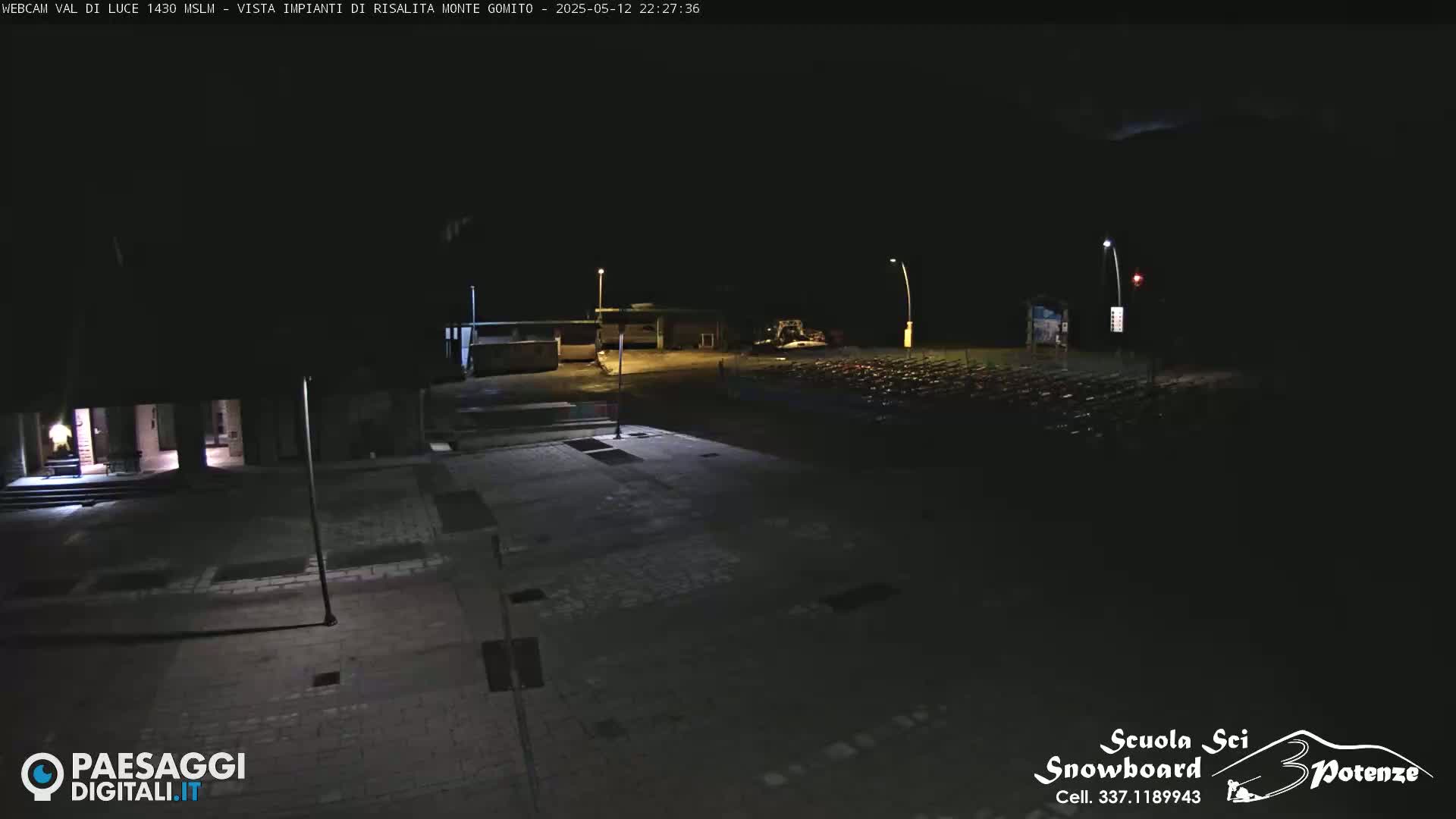 A nighttime, outdoor view of a paved area with a building and what appears to be a parking lot of objects.