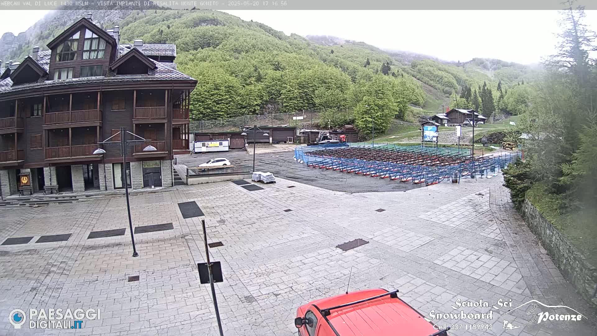 A stone plaza sits in front of a multi-story brown building, with rows of what appear to be snow sports equipment in the background under an overcast sky.