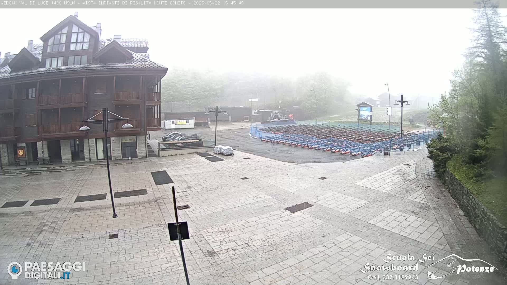 A stone plaza with a multi-story building and rows of what appear to be snowboard or ski racks is visible in foggy conditions.