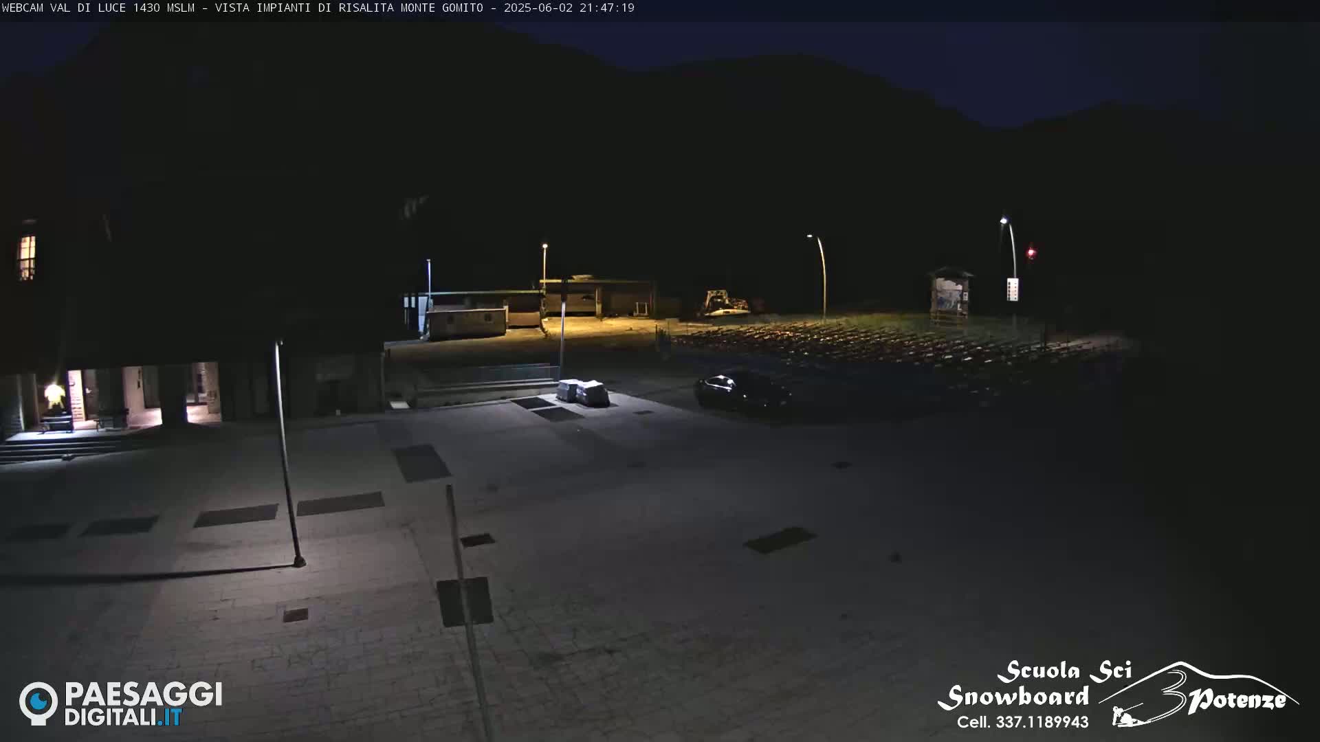 A nighttime, dimly lit, paved area with buildings and a few vehicles, under a dark sky.