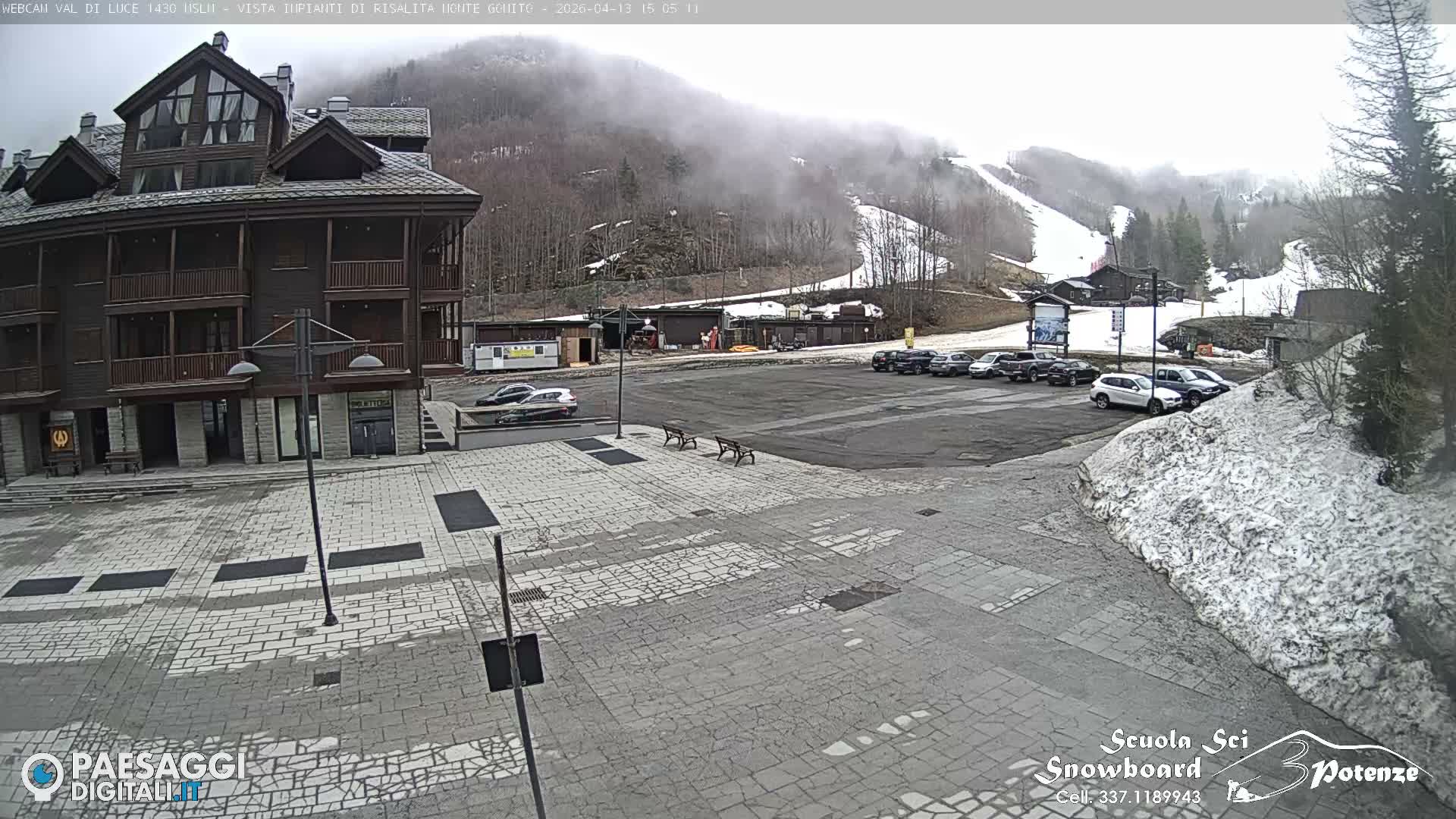A multi-story building and a busy parking lot are visible amidst a snowy landscape on a heavily fogged winter day.