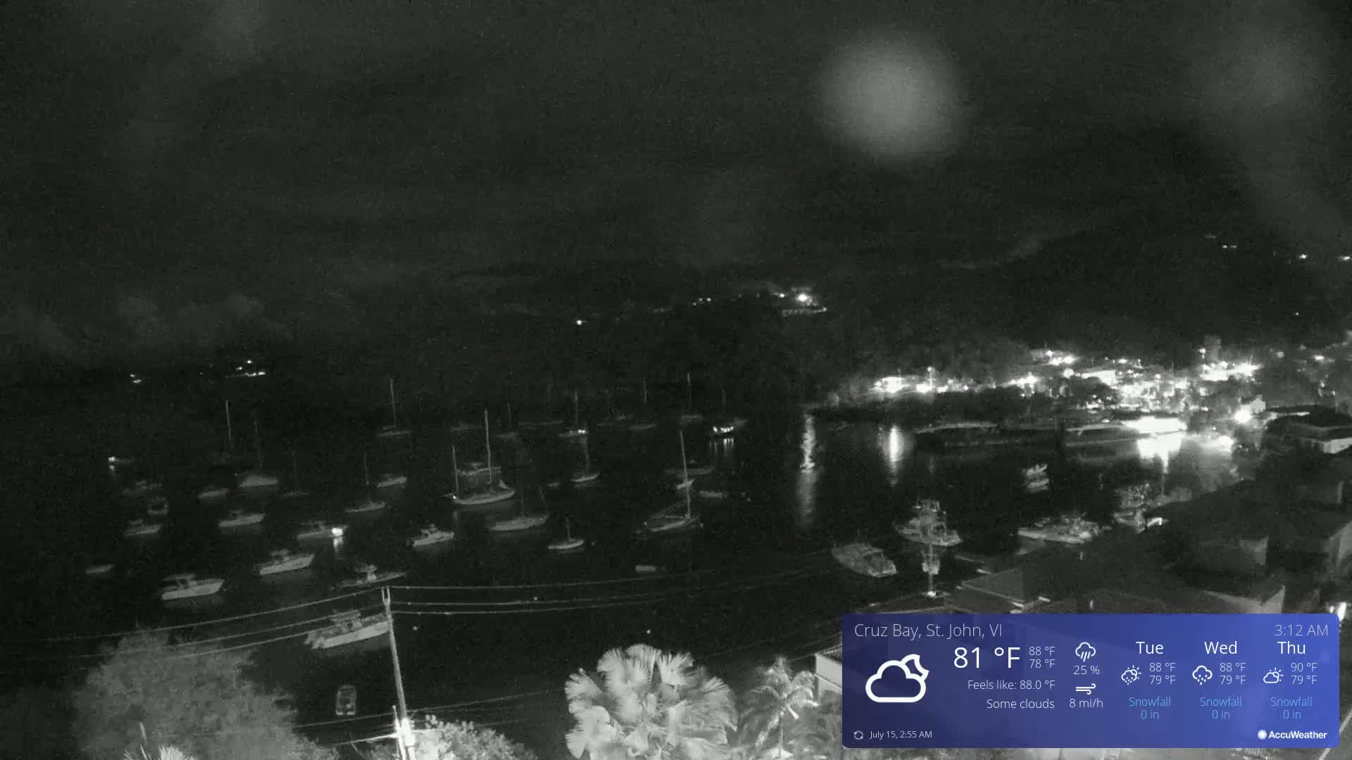 A nighttime view of a harbor filled with numerous boats under a dark sky with some clouds and a light rain.