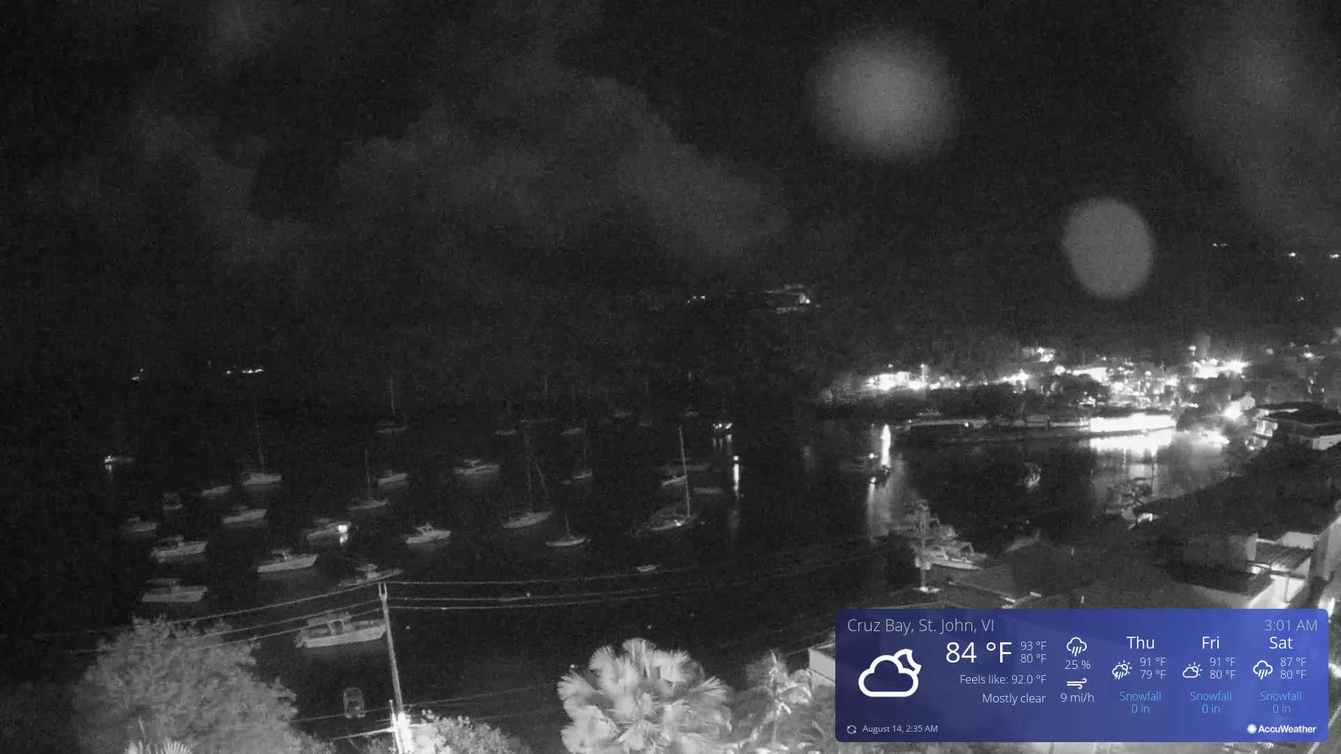 A nighttime view of a harbor filled with boats under a mostly clear sky with light cloud cover.
