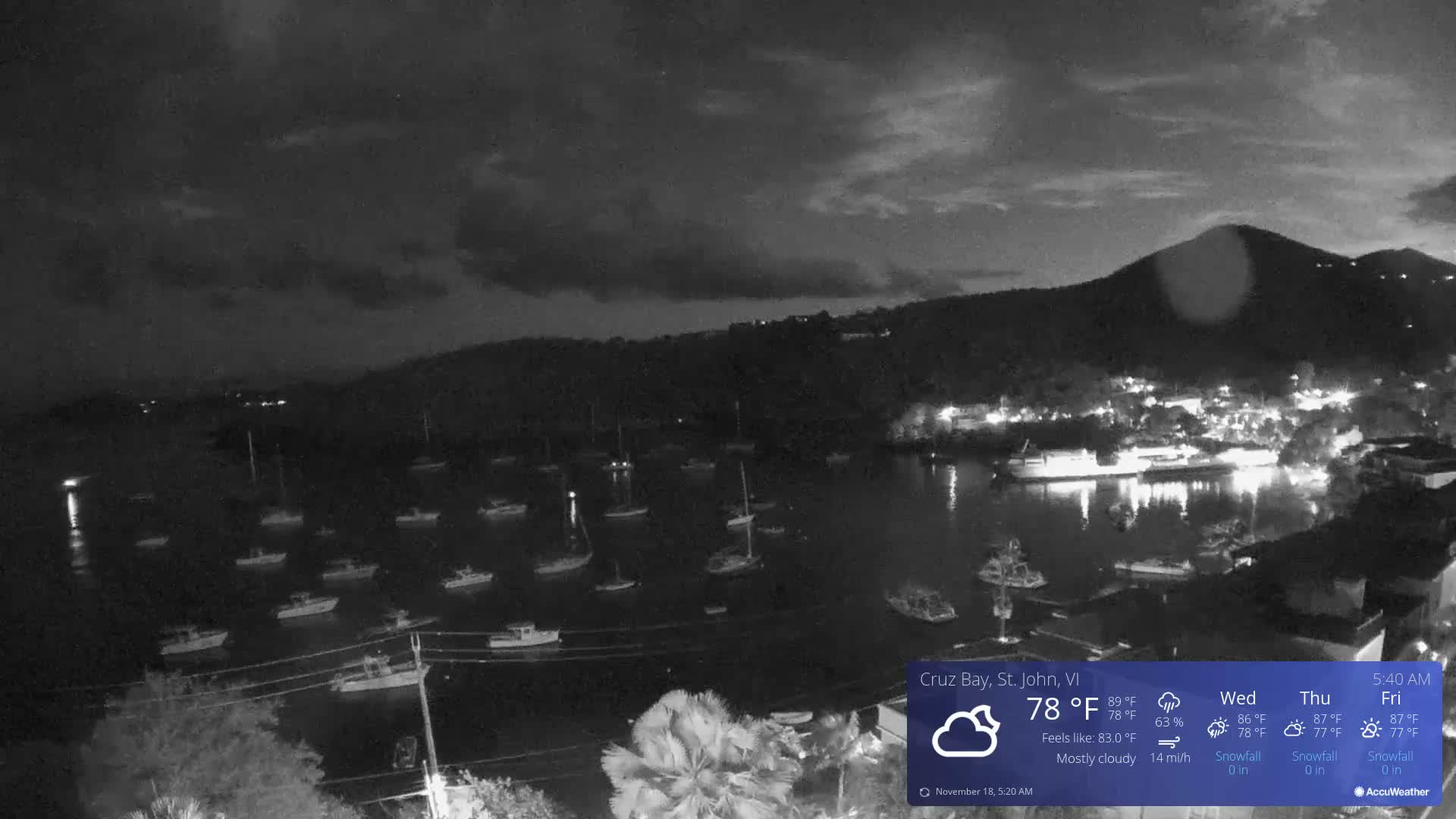 The image captures a nighttime view of a bay or harbor filled with numerous boats, with lights from the shore reflecting on the water, under a mostly clear sky.