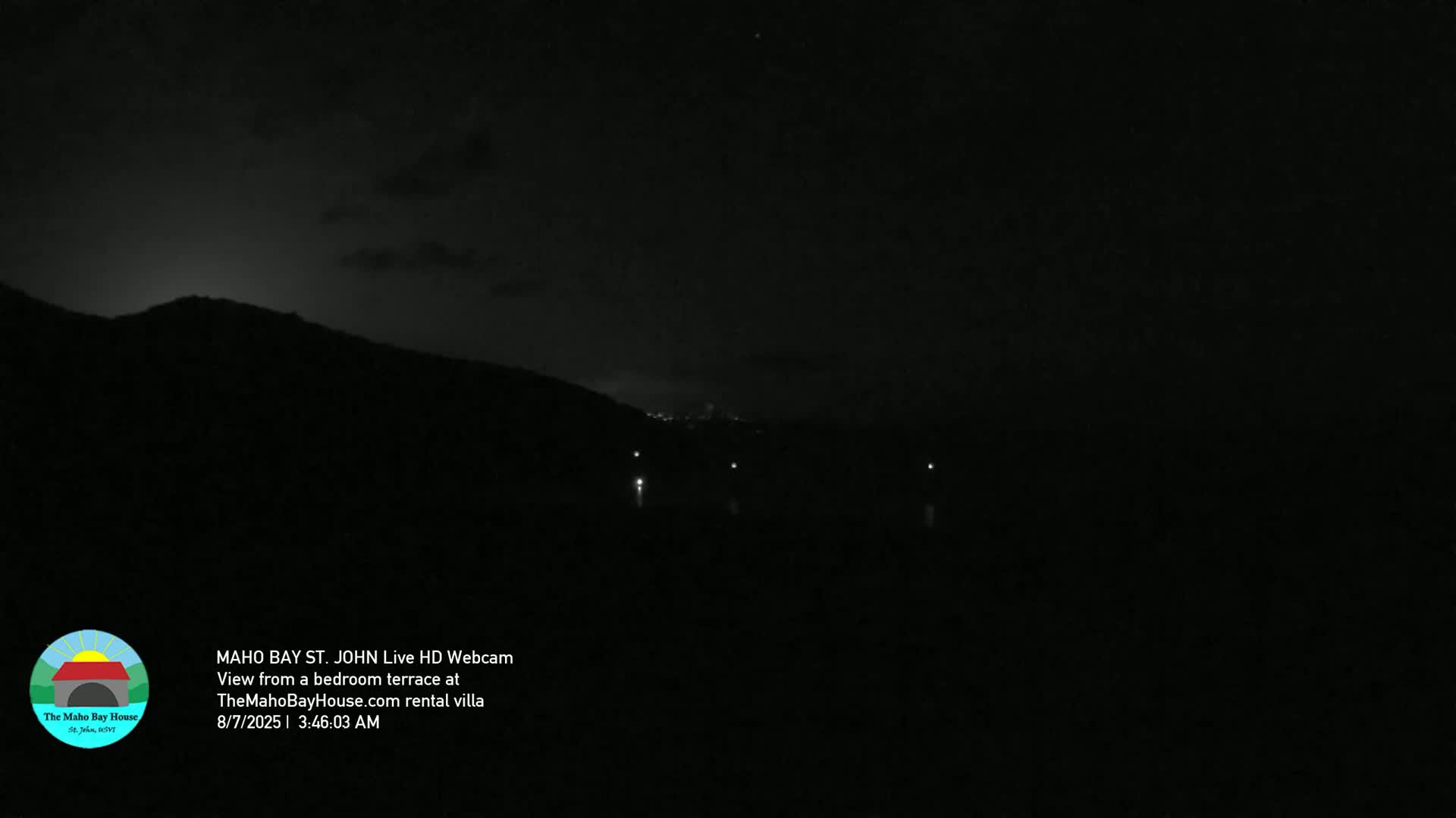 A nighttime view from a terrace shows a dark, silhouetted hillside with a few distant lights visible under a mostly clear, dark sky.