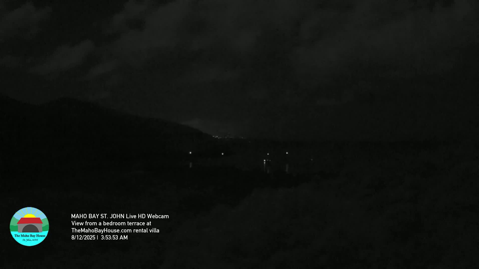 A dark nighttime scene shows dimly lit hills and a few distant lights under a cloudy sky.