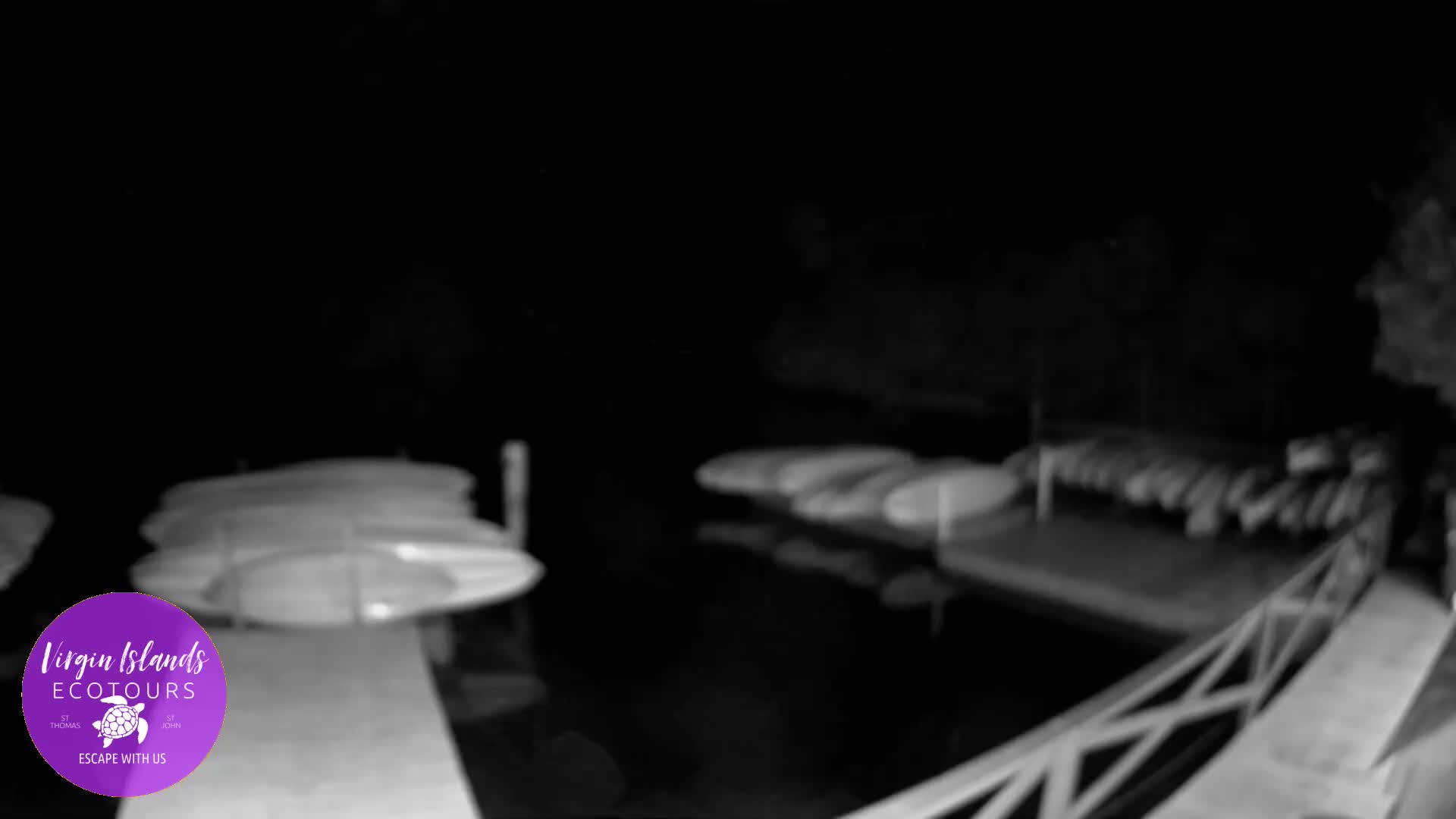 On a clear night, the image captures a dark body of water flanked by two docks, each laden with stacks of kayaks or paddleboards.
