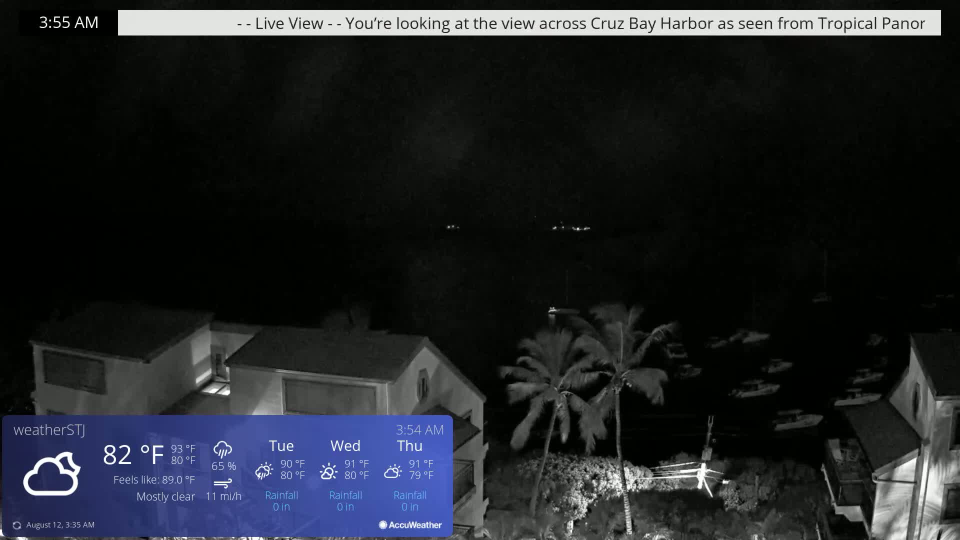 A nighttime, mostly clear view of a harbor with some boats and palm trees, under a dark sky.