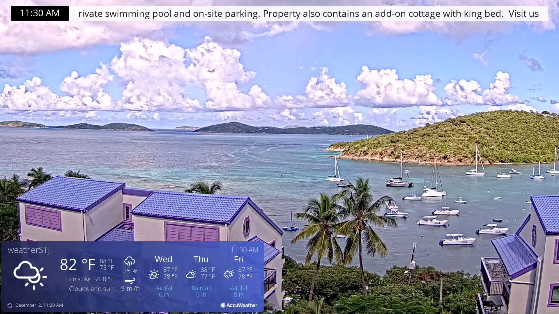 On a partially cloudy day with blue skies, a tropical bay is filled with numerous sailboats anchored in clear turquoise waters, bordered by lush green islands and a vibrant house with a purple roof and palm trees in the foreground.