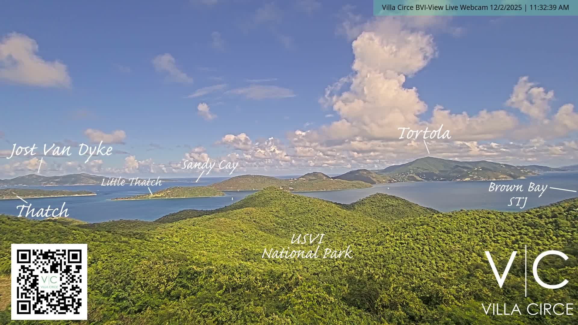 The scene captures a beautiful, sunny panoramic view of multiple verdant tropical islands emerging from clear blue ocean waters, with scattered white clouds across a bright blue sky, and dense green hills dominating the foreground.