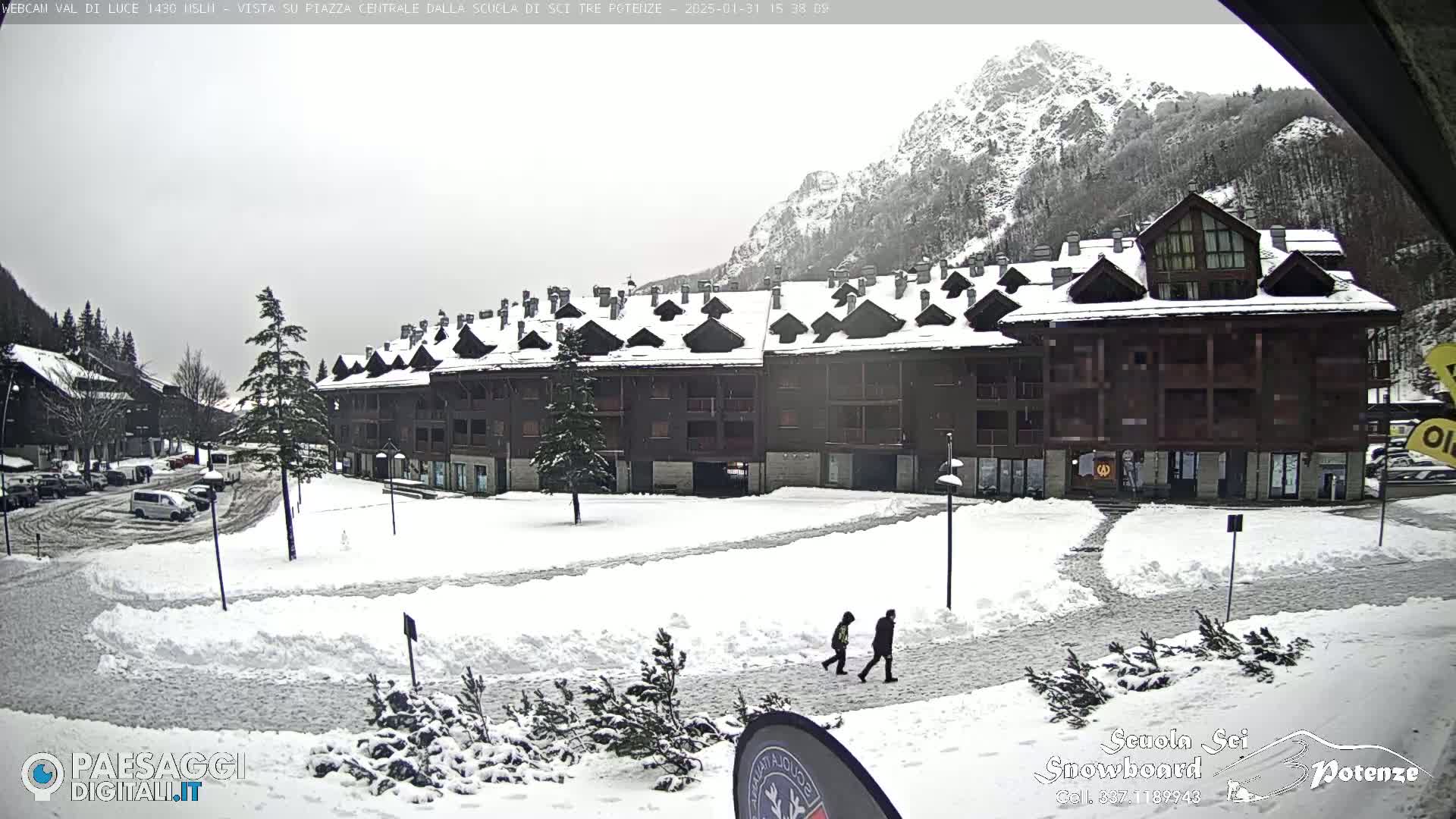 A snow-covered plaza with a large building and mountains in the background, under an overcast sky.