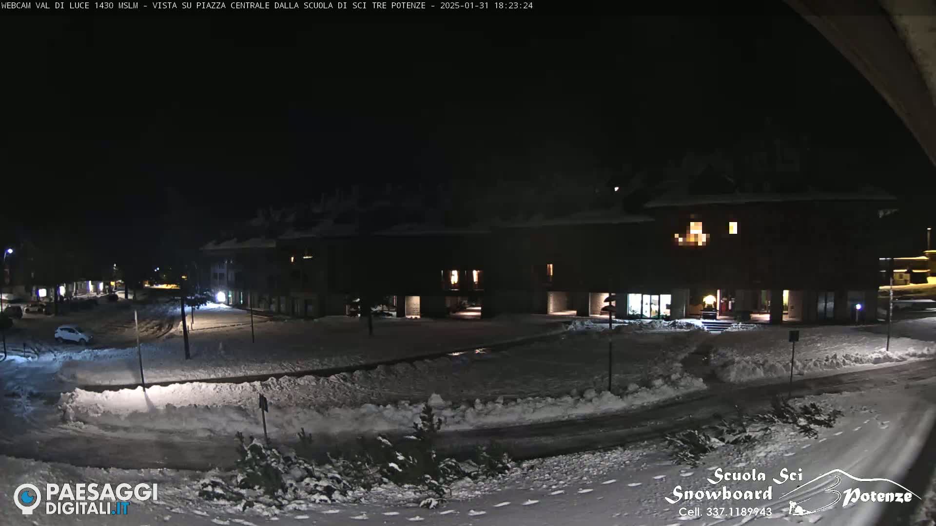 A snow-covered town square at night, illuminated by dim lights from nearby buildings.