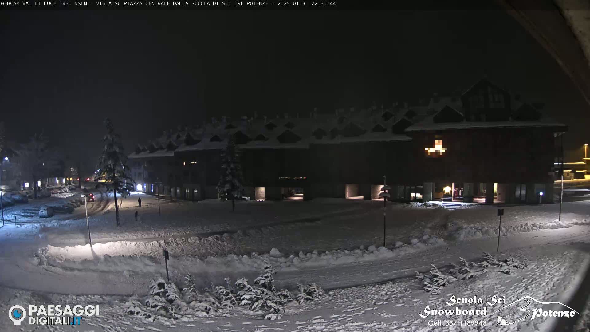 A snow-covered plaza at night, illuminated by building lights, with a large building in the background.
