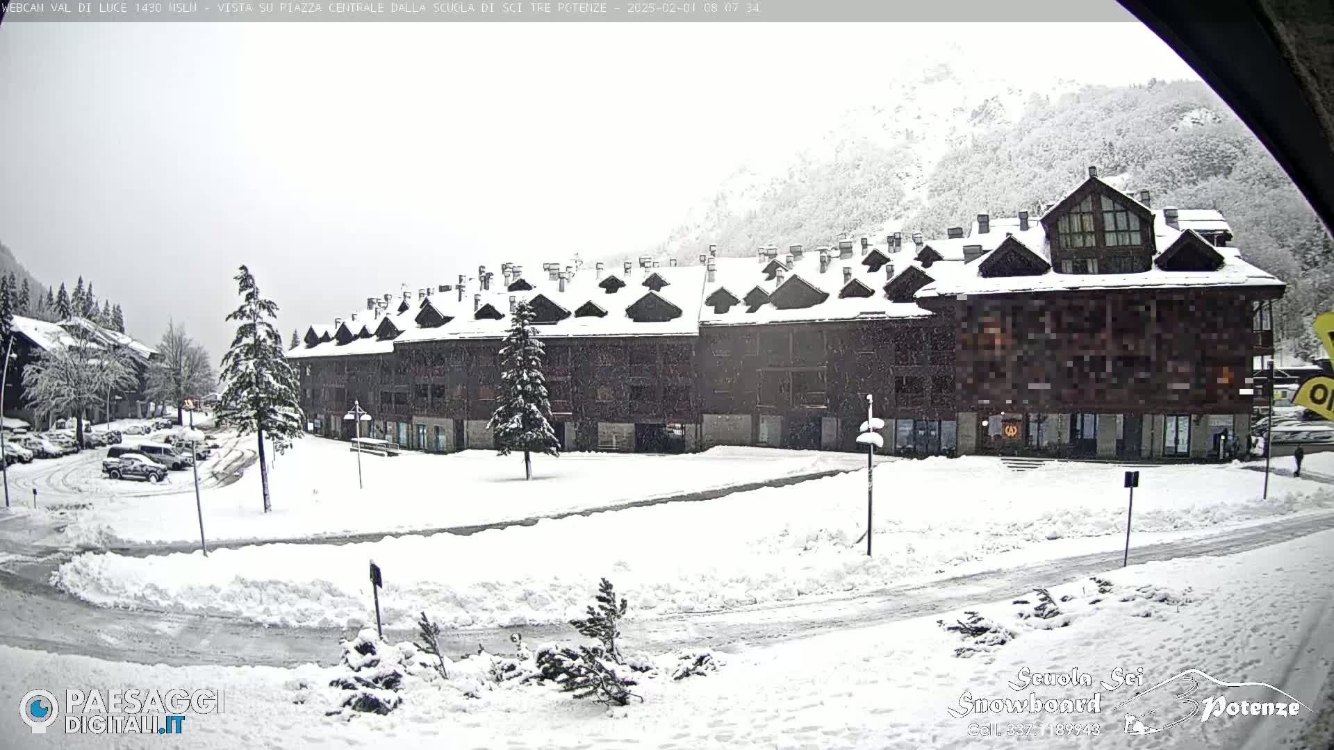 A snow-covered plaza sits in front of a multi-story building nestled in a snowy mountainside.