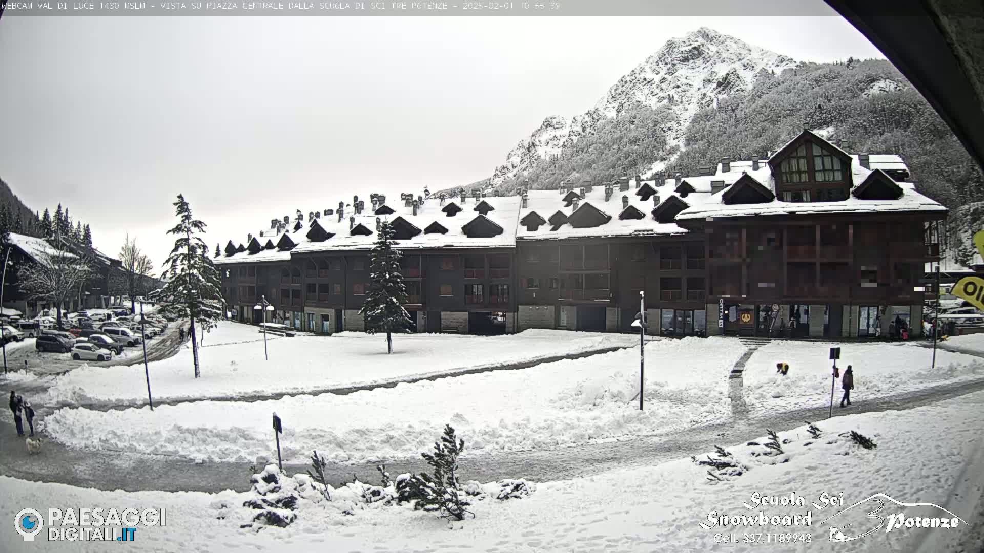 A snow-covered plaza with a large building and a mountain in the background, under overcast skies.