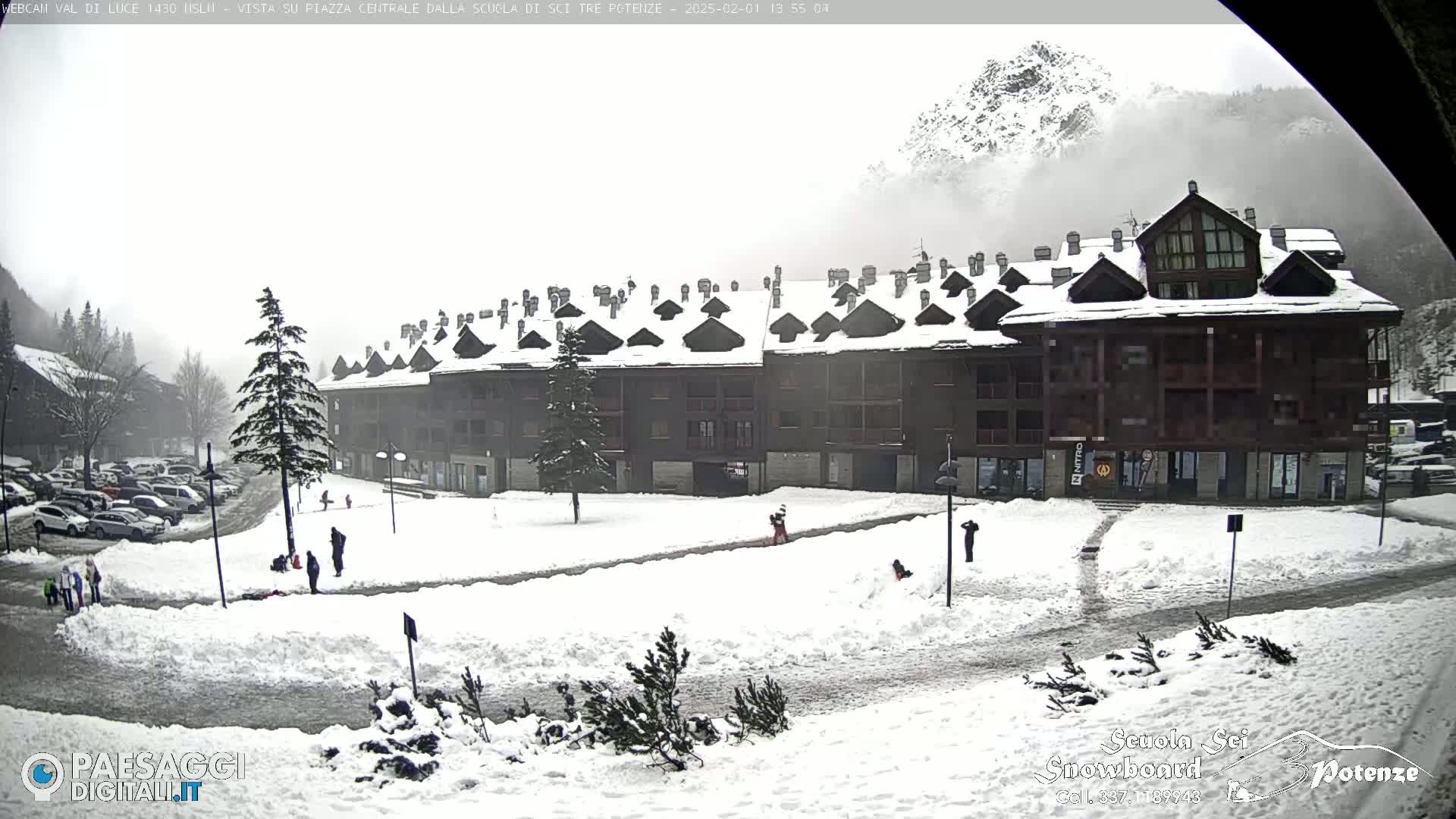 A snow-covered plaza sits in front of a multi-story building in a mountainous area under foggy conditions.