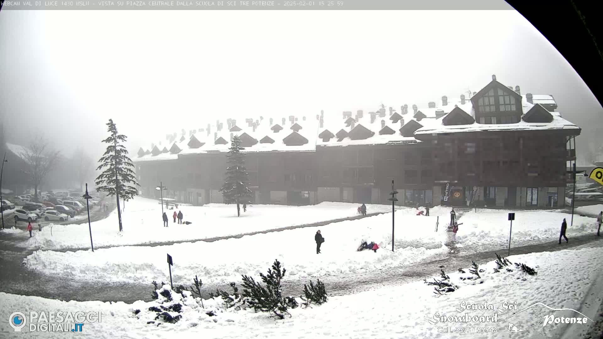 A snow-covered plaza in front of a multi-story building is shrouded in fog, with a few people visible.