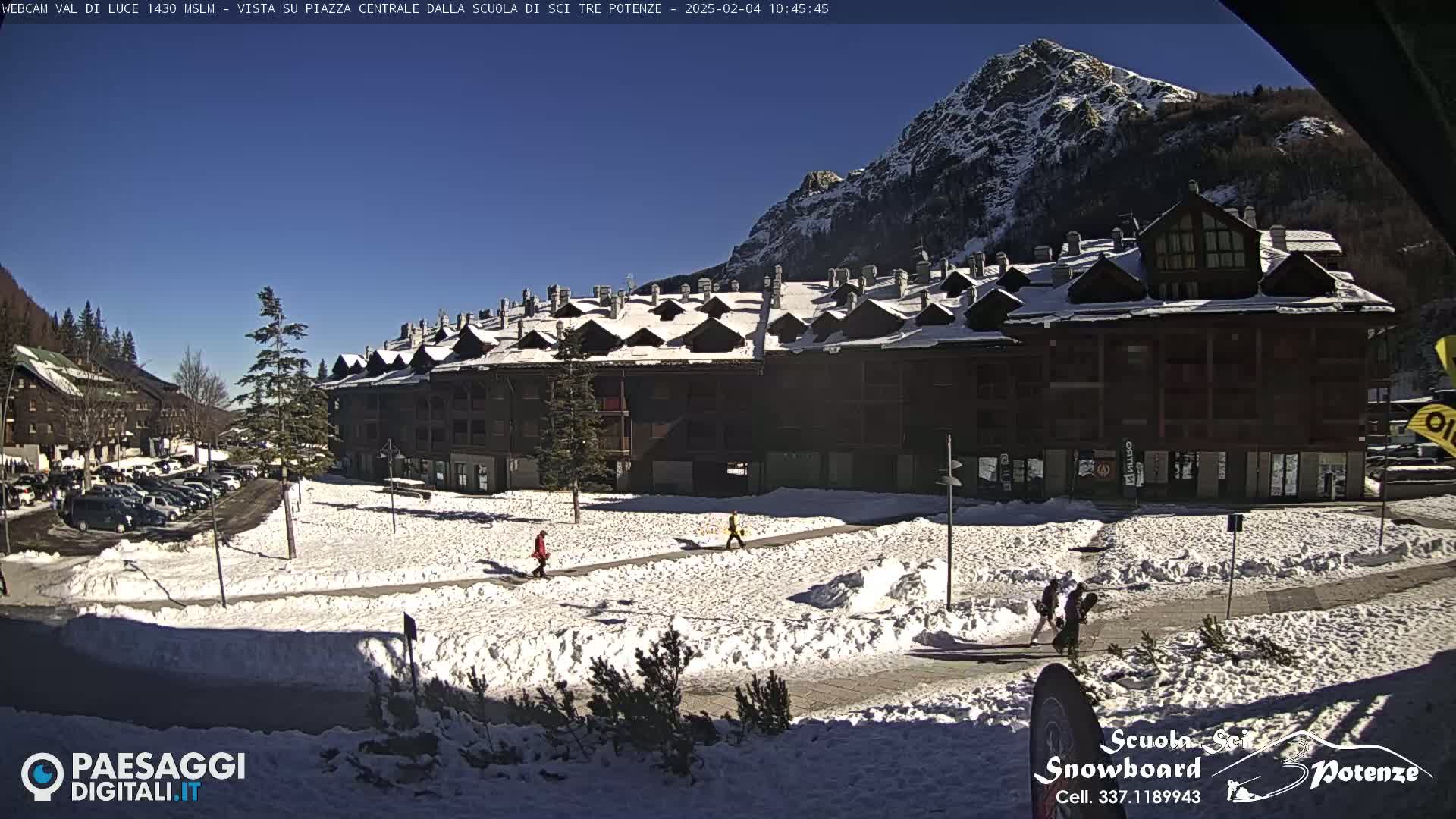 A snow-covered plaza with a large building and mountains in the background under a sunny sky.