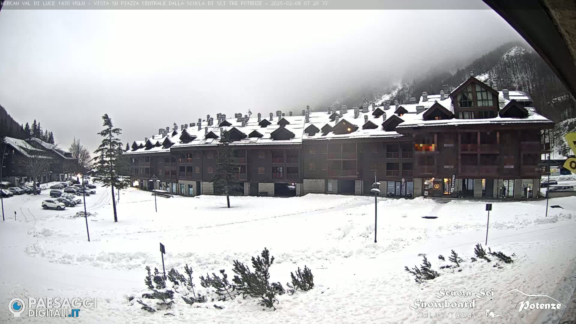 A snow-covered plaza sits in front of a multi-story brown building under an overcast sky.