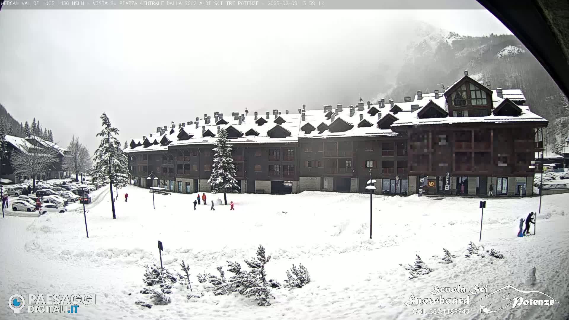 A snow-covered plaza sits in front of a large, multi-story building in a mountainous region under an overcast sky.
