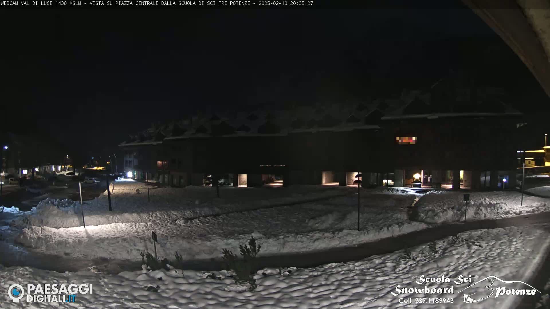 A snow-covered plaza at night, illuminated by building lights, is seen from a vantage point overlooking a building complex.