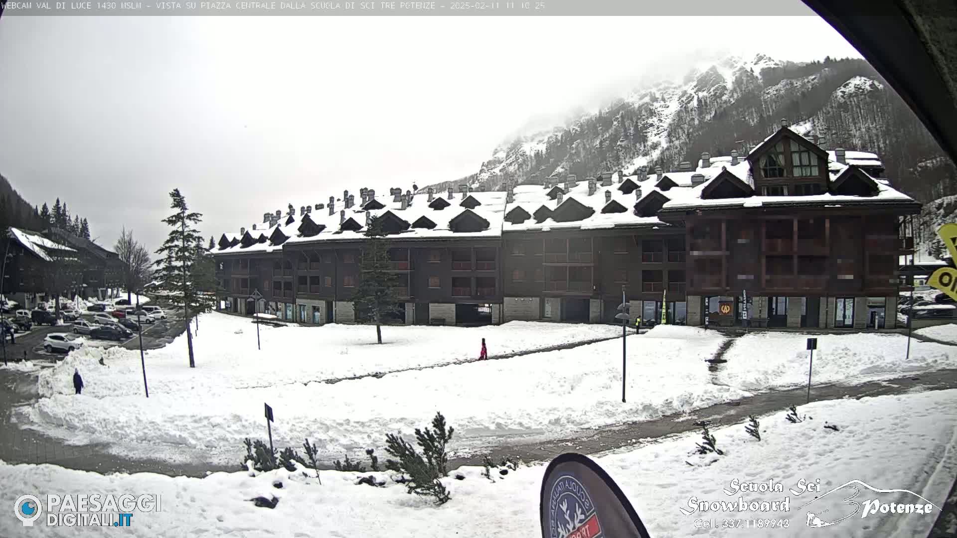 A snow-covered plaza in front of a multi-story building in a mountainous area under an overcast sky.
