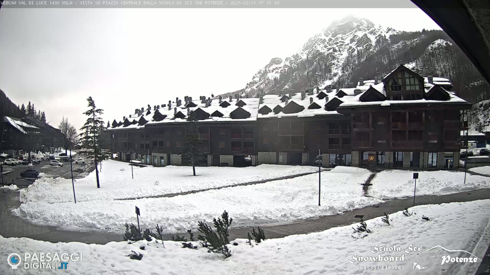 A snow-covered plaza with a multi-story building and a mountain in the background under an overcast sky.